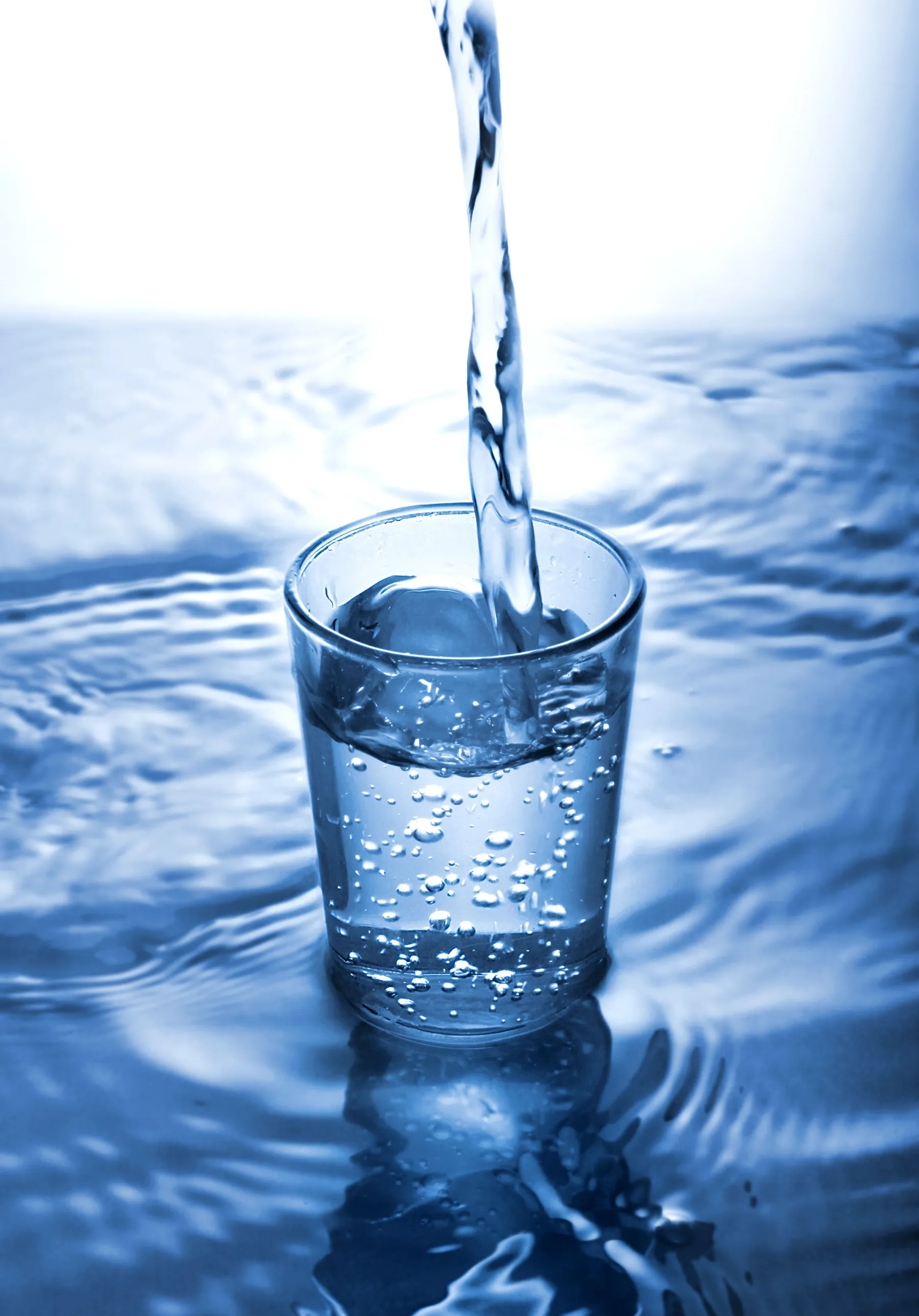 Vaso de agua llenándose sobre una superficie con ondas