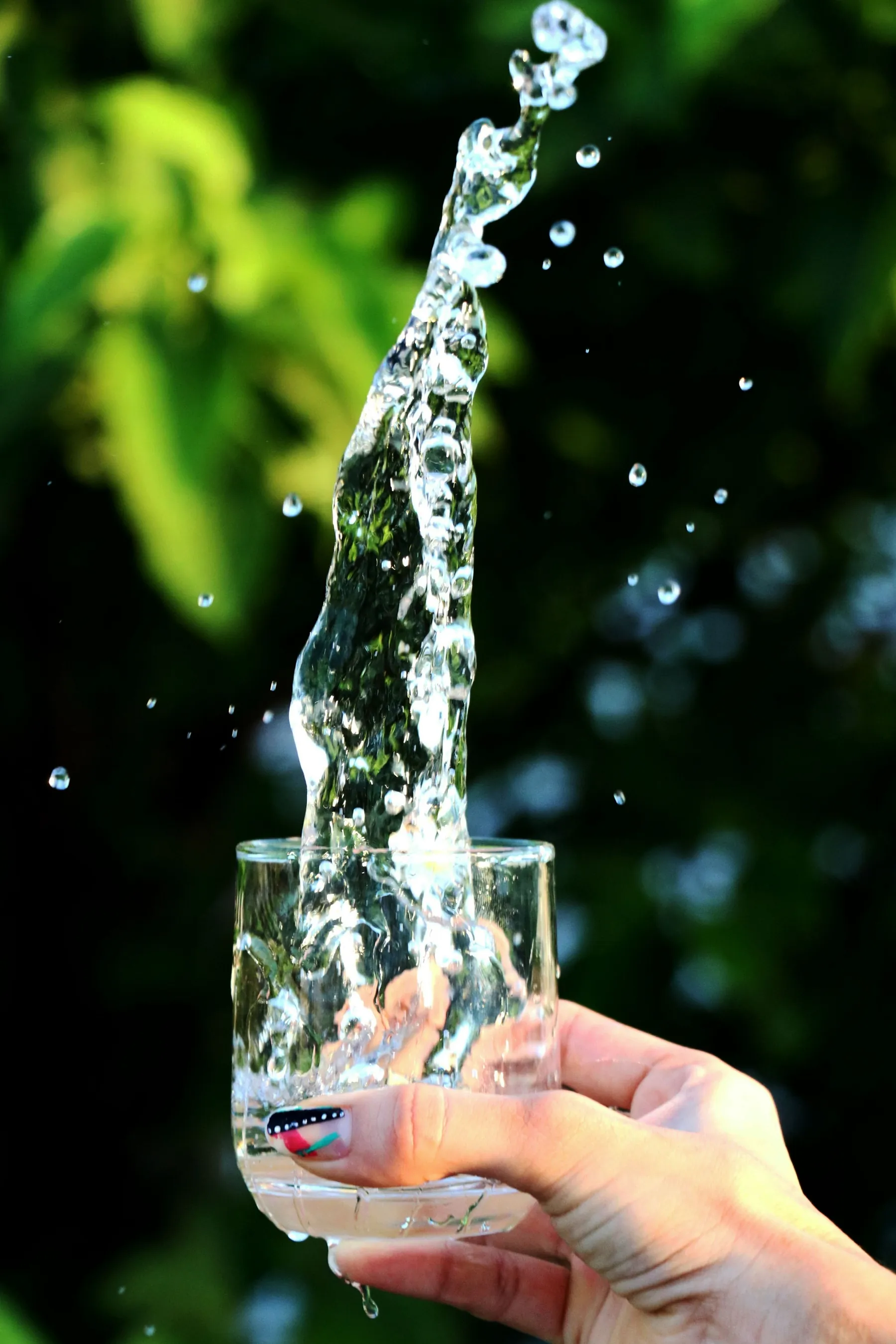 Mano sosteniendo un vaso de agua que salpica con vegetación al fondo